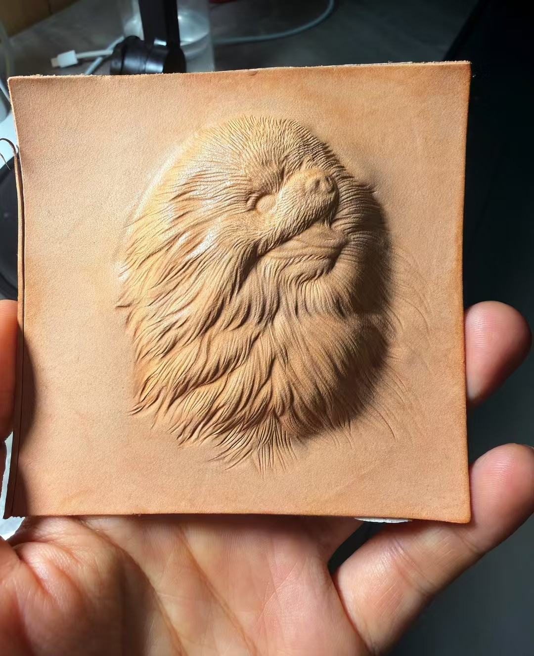 Unpainted dog portrait relief in a leather sheet, showing carved fur texture