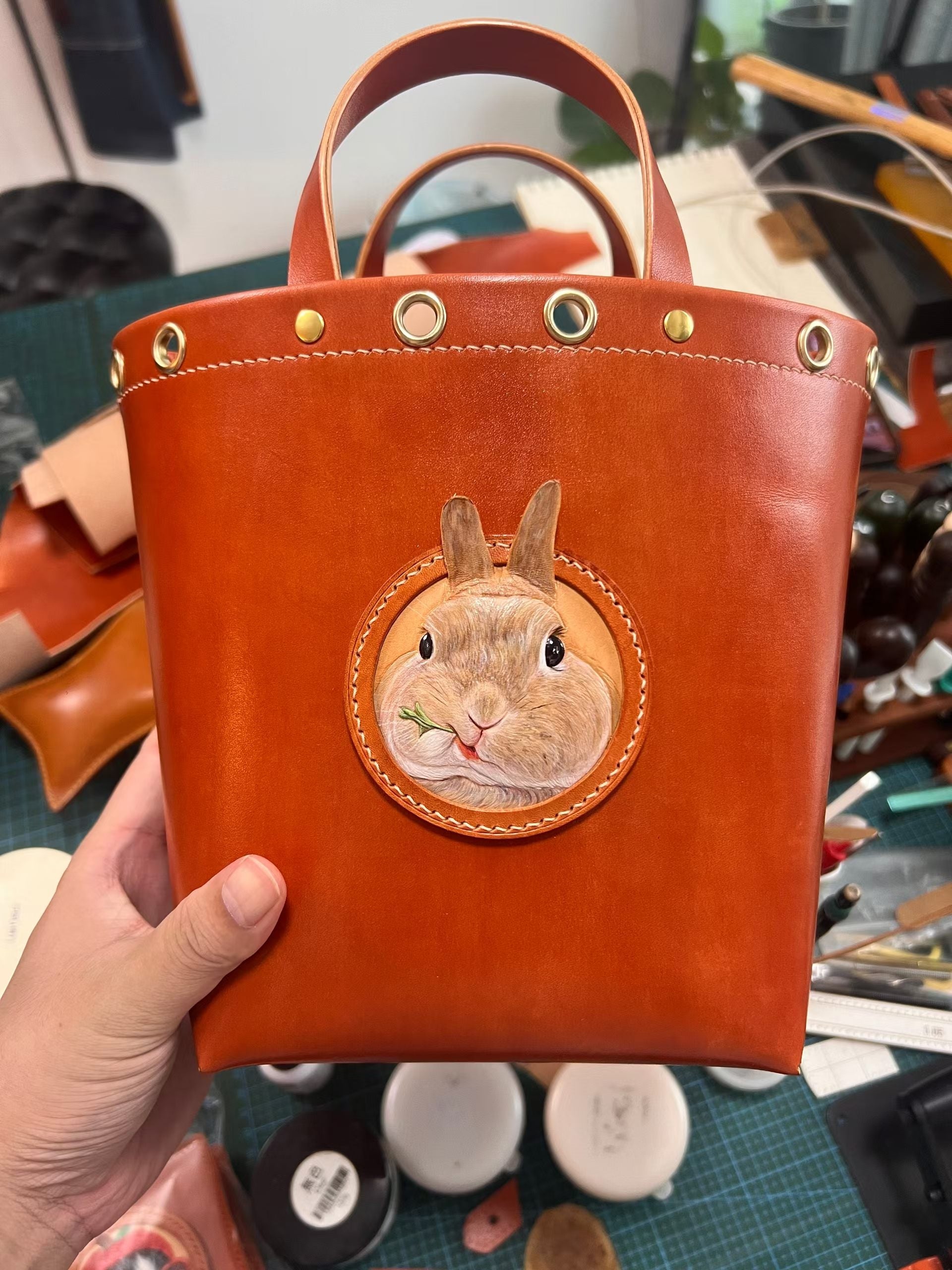 Supplier photograph of an orange leather tote with a rabbit portrait and brass-coloured fittings.